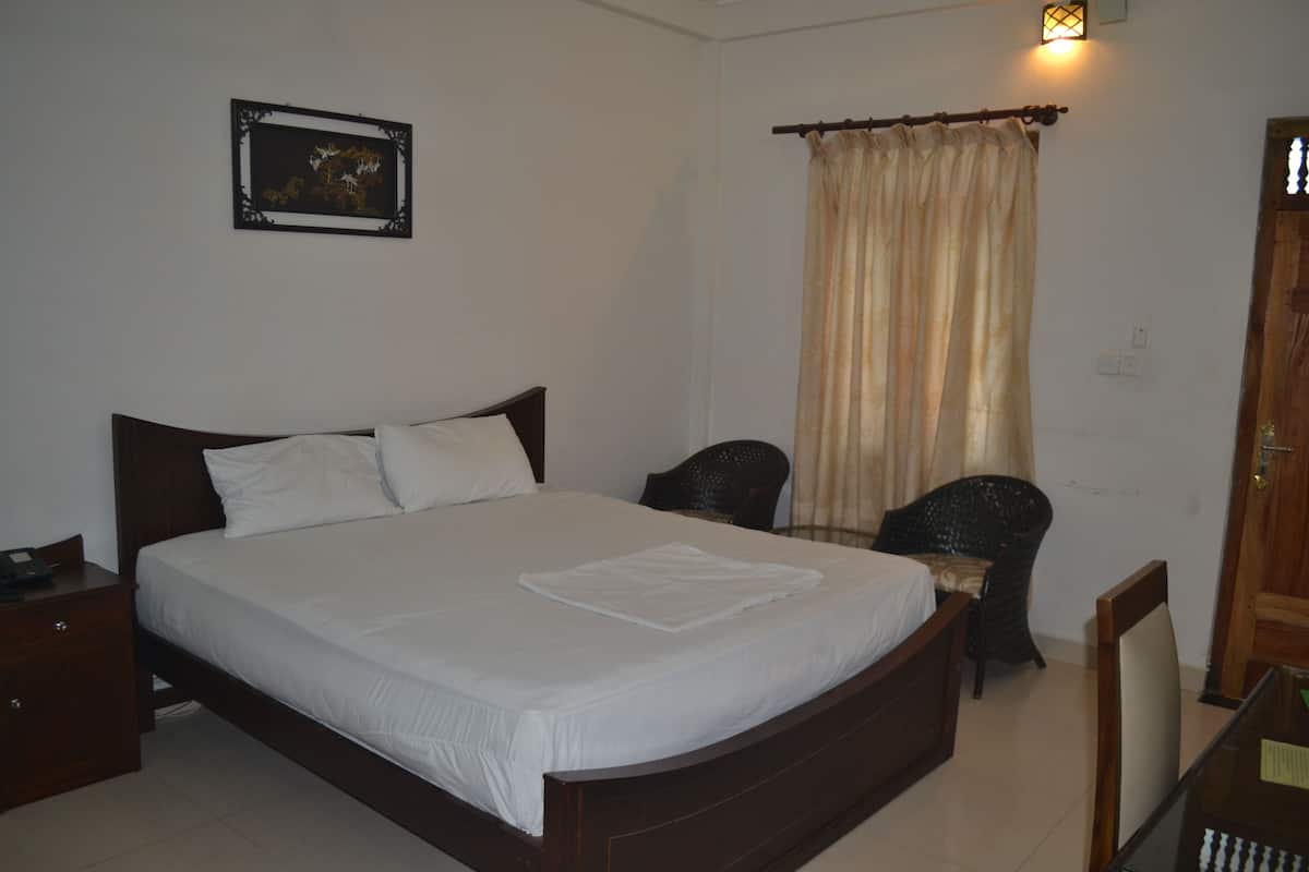 A neatly made bed with white linens, a wooden headboard, a bedside table with a phone, a chair, and a wall-mounted picture.