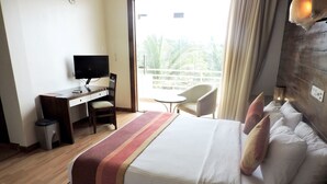 Habitación de hotel con cama, escritorio con televisor, silla y balcón con vista a palmeras.