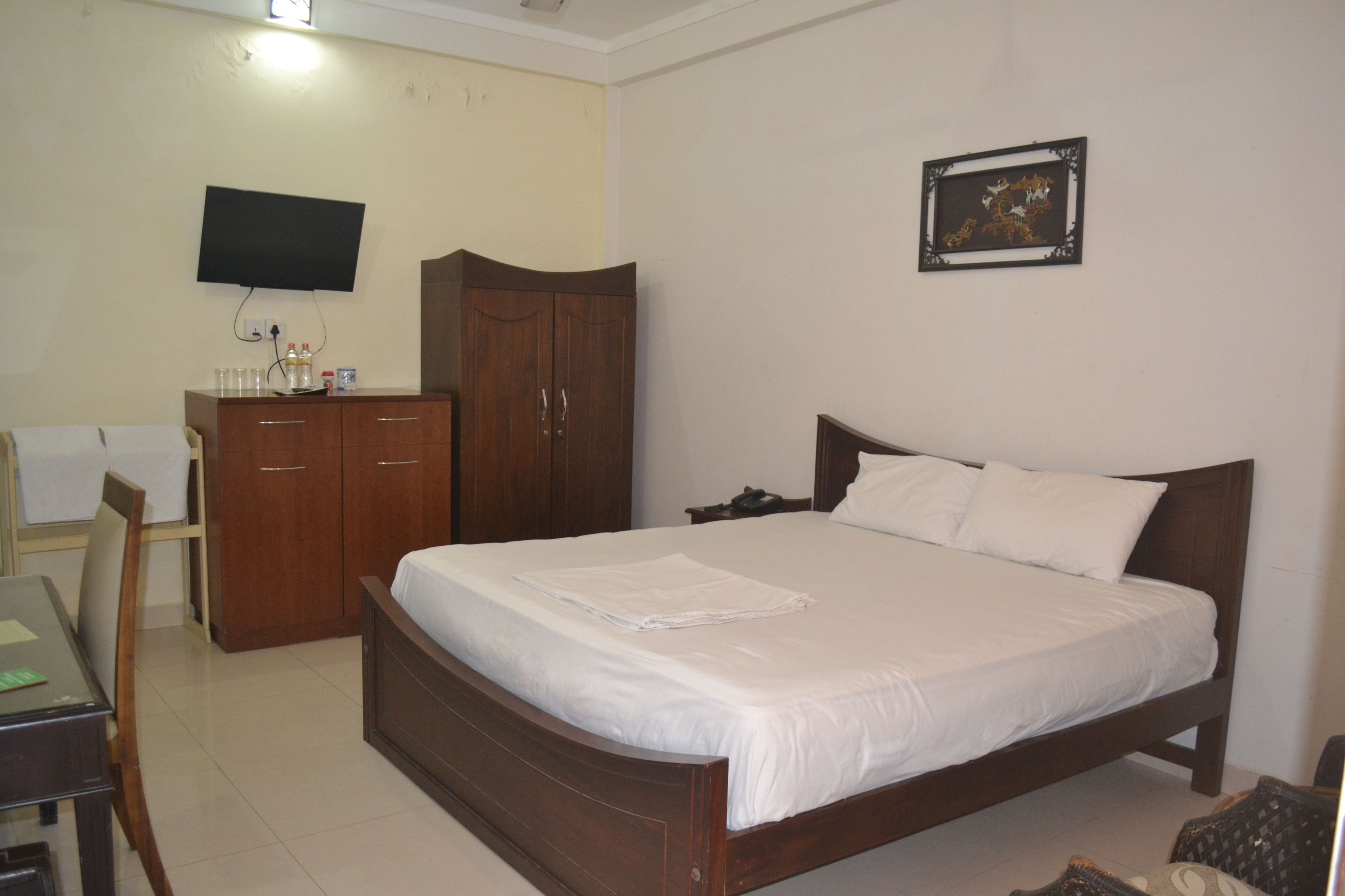A hotel room with a bed, a desk, a wardrobe, a television, and a framed picture on the wall.