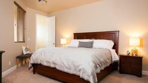 Un dormitorio con una cama grande, dos mesitas de noche con lámparas, una puerta y una ventana con persianas.
