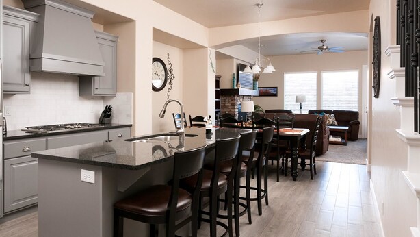 Una cocina moderna con una isla central, taburetes de bar y una zona de comedor con sofá y mesa.