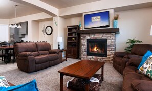 A living room with a stone fireplace, leather sofas, a wooden coffee table, and a television above the fireplace.