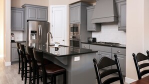 Una cocina moderna con gabinetes grises, electrodomésticos de acero inoxidable y una isla central con taburetes de bar.