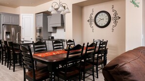 Un comedor con mesa y sillas de madera, una cocina al fondo y un reloj de pared.