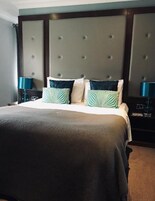 Una habitación de hotel con una cama grande, un cabecero capitonado y dos mesitas de noche con lámparas.