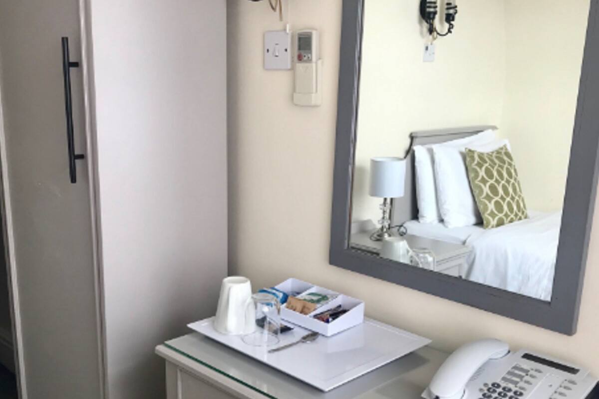 A hotel room with a desk, a telephone, a mirror, and a chair.