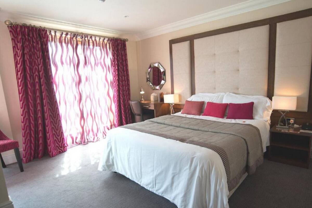 A hotel room with a large bed, a nightstand, a chair, and a window with curtains.