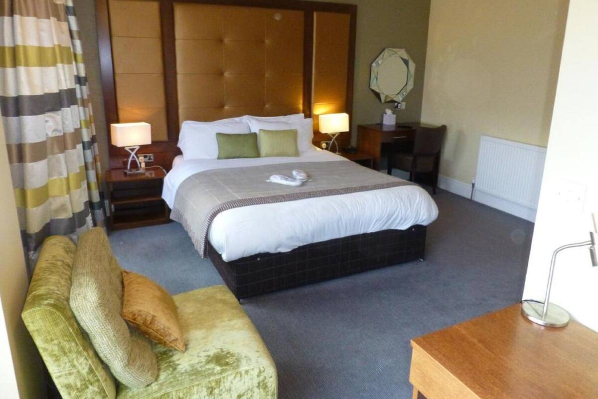 A hotel room with a large bed, two bedside tables, a bedside lamp, a chair, a small table, and a mirror on the wall.