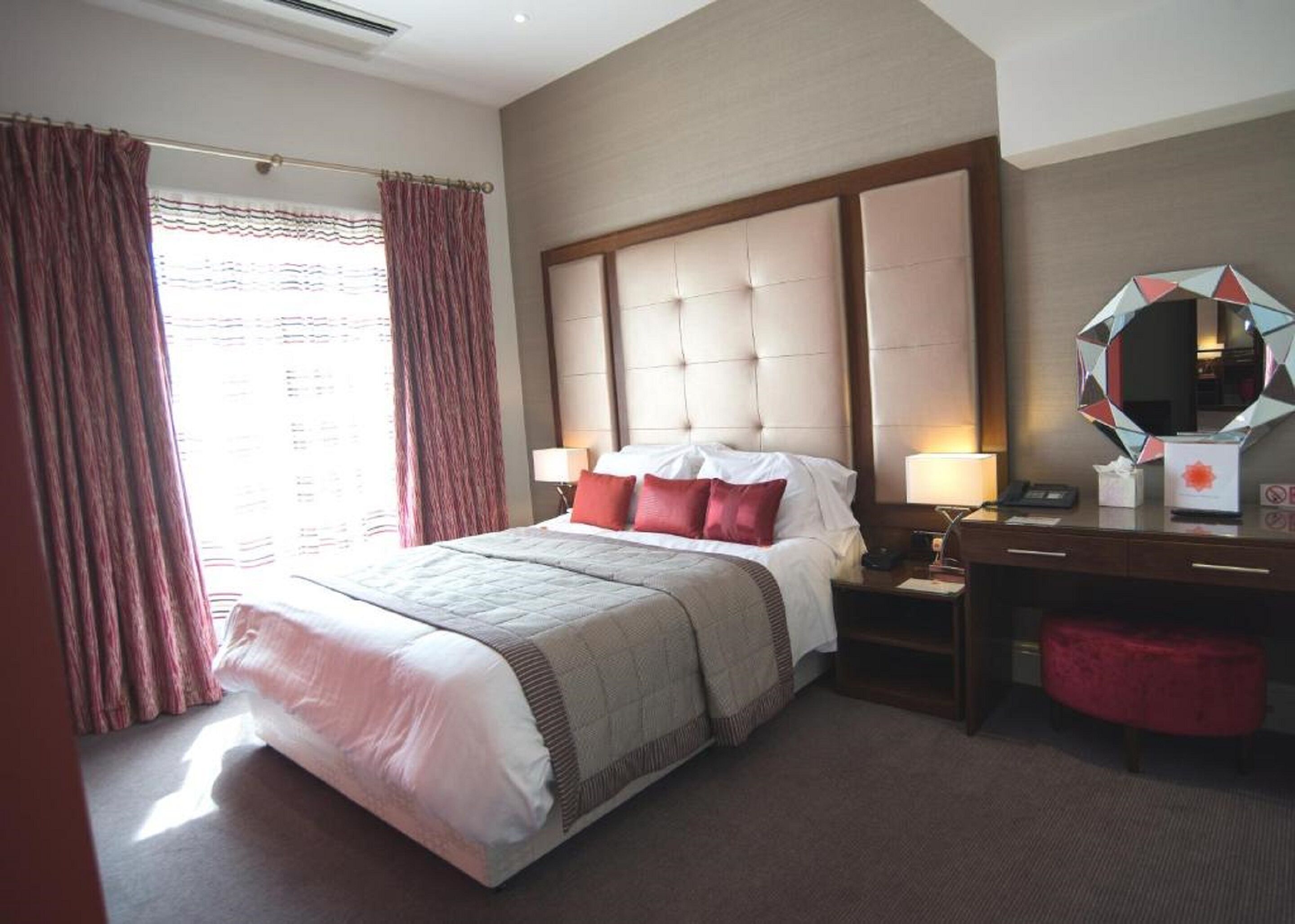 Quarto de hotel com uma cama grande, mesa de cabeceira com abajur, cômoda e espelho.