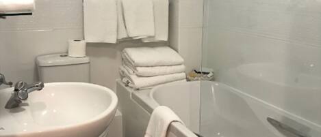 Une salle de bain avec un lavabo, des toilettes et une baignoire. Des serviettes sont pliées sur le bord de la baignoire et un rideau de douche est installé.