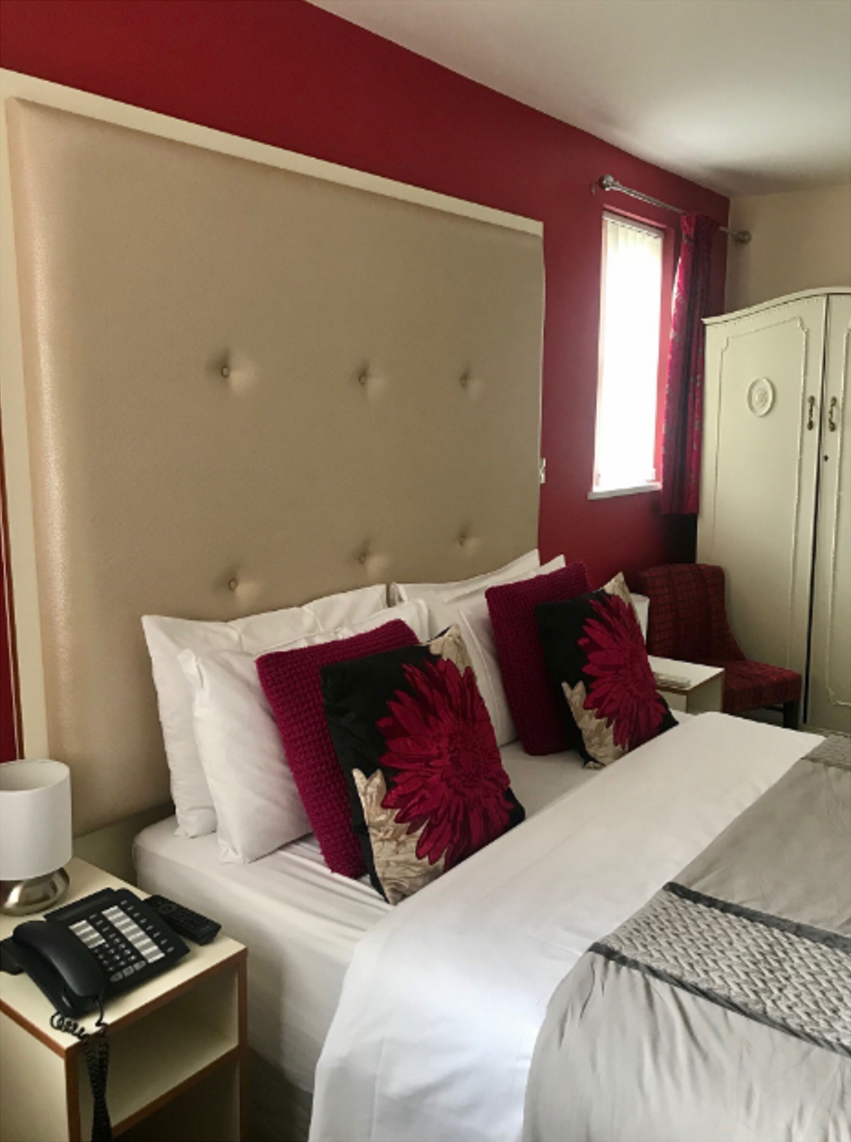 A hotel room with a bed, a bedside table with a phone, a wardrobe, and a window with curtains.