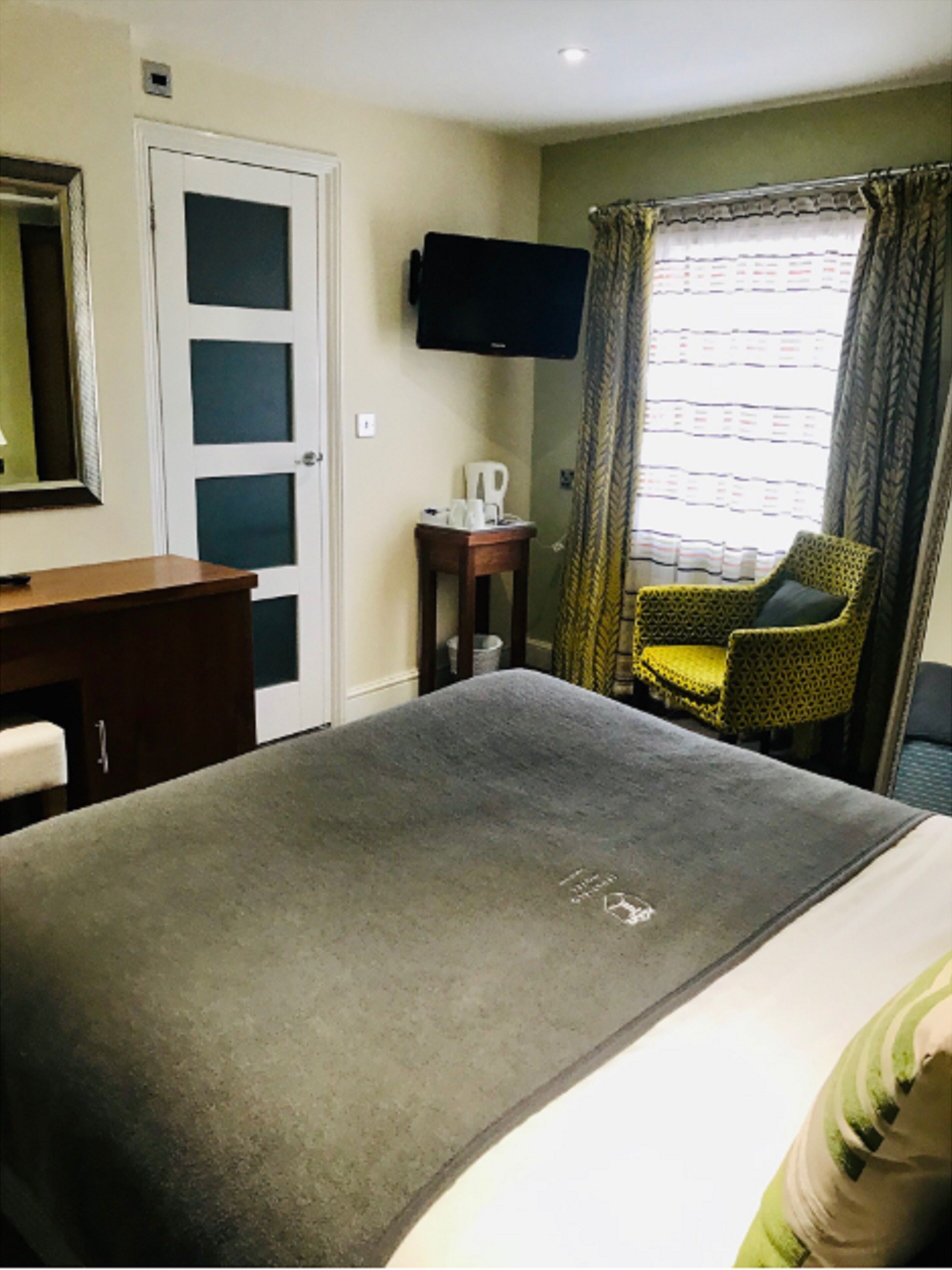 Une chambre d’hôtel équipée d’un lit, d’un bureau, d’une chaise, d’une télévision et d’une fenêtre avec des rideaux.