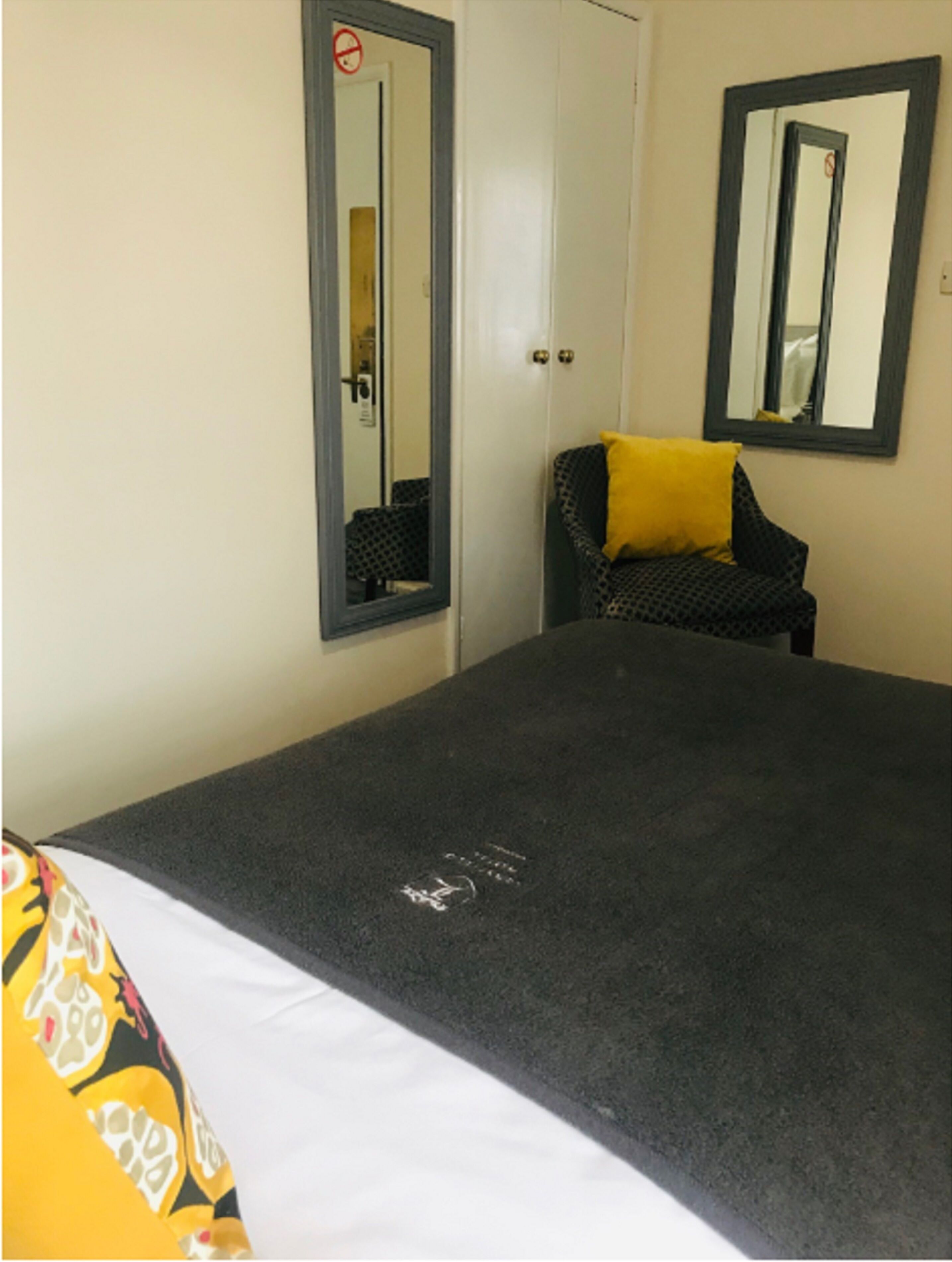 A bedroom with a bed, a chair with a yellow pillow, and two mirrors on the wall.