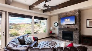 A living room with a stone fireplace, leather sofa, and a television mounted above it. - Coral Vista Villa (Washington)