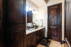 A bathroom with dark wooden cabinets, a vanity with a mirror, and a door with a light fixture above it. - Endless Summer (Washington)