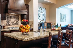 A kitchen with granite countertops, a fruit bowl, a sink, and wooden chairs. - Endless Summer (Washington)
