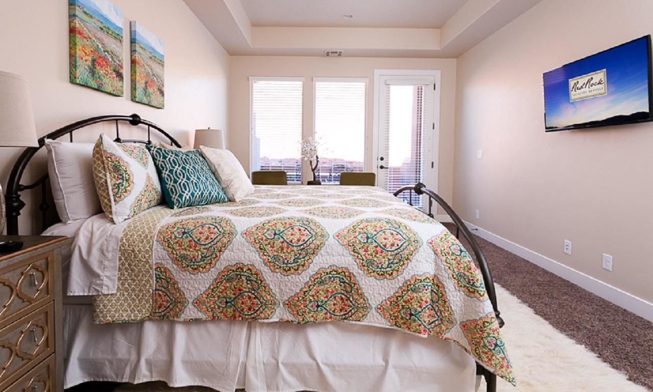 A bedroom with a bed, a dresser, a TV, and a window with blinds.