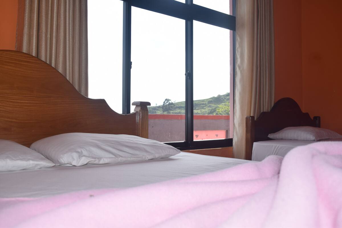 A hotel room with a large window, a bed with white bedding, and a view of a building outside.