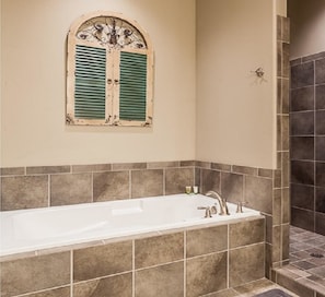 A bathroom with a bathtub, a window with green shutters, and tiled walls.