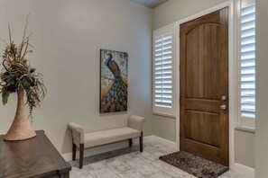 A hallway with a wooden door, a bench, a painting of a peacock, and a plant on a table. - Golfer's Dream (Washington)