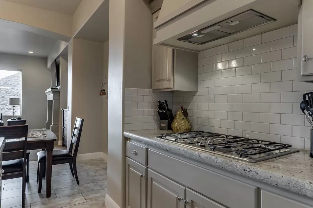 Una cocina con salpicadero de azulejos blancos, estufa a gas y comedor con mesa y sillas.