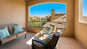 A balcony with a sofa and chairs, a view of neighboring houses, and a clear sky.