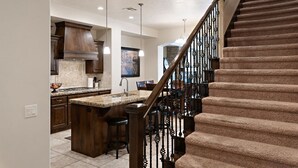A modern kitchen with a central island, dark wood cabinets, and a staircase with a decorative railing.