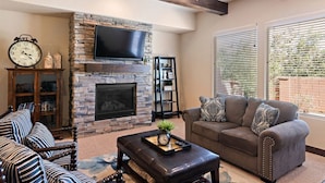 A living room with a stone fireplace, a flat-screen TV, a sofa, a coffee table, and a bookshelf.