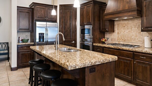 A kitchen with dark wood cabinets, granite countertops, stainless steel appliances, and bar stools.