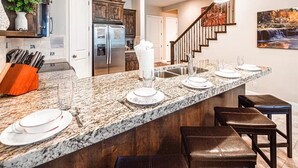 A kitchen with granite countertops, a stainless steel refrigerator, and a wooden staircase. - Pebble Beach (Washington)