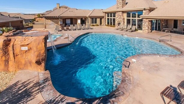 A swimming pool with a rock feature, lounge chairs, and a stone building with a tiled roof. - Pebble Beach (Washington)