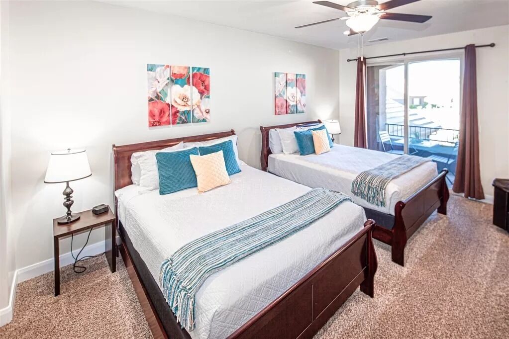 A bedroom with two beds, a ceiling fan, and a view of the outdoors.