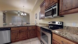 Una cocina con armarios de madera, lavavajillas de acero inoxidable, microondas, estufa y encimera de granito.
