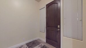 Un corridoio con una porta in legno, una parete bianca e un tappeto decorato.