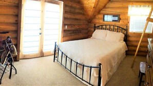 A wooden cabin bedroom with a bed, a small table, and a window. - Red Rock Ranch Cabin (Escalante)