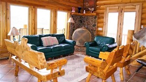 A cozy log cabin interior with a green leather sofa, wooden chairs, and a stone fireplace. - Red Rock Ranch Cabin (Escalante)