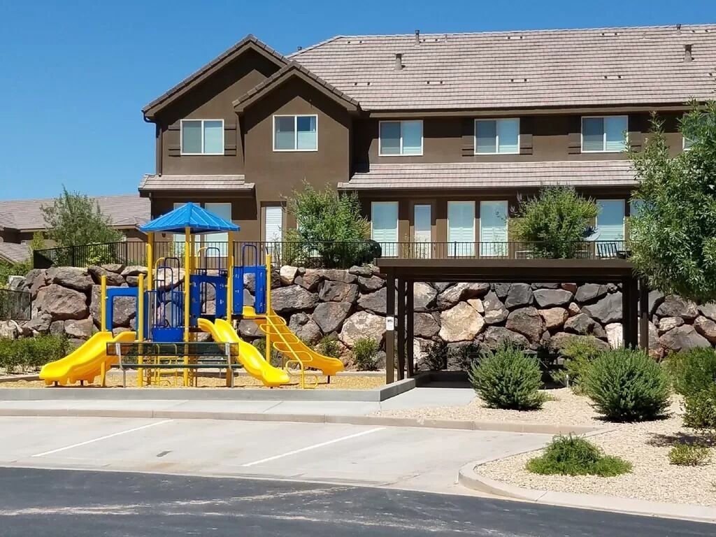 A residential building with a playground featuring slides and a blue-roofed shelter.