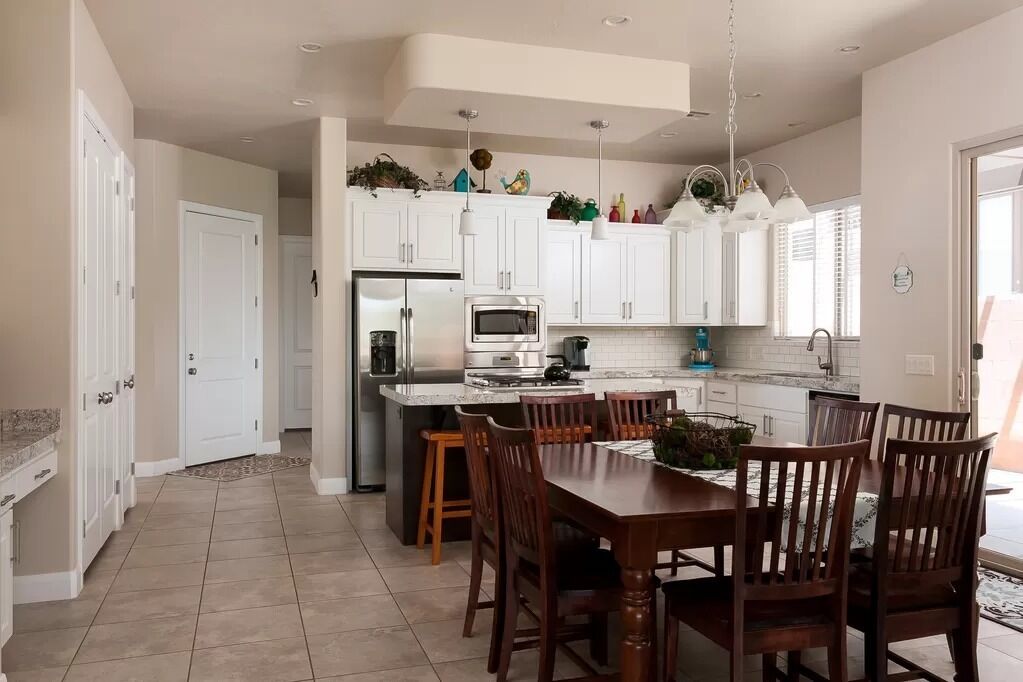 A modern kitchen with white cabinets, a dining area with wooden chairs, and a built-in island with a microwave and toaster.