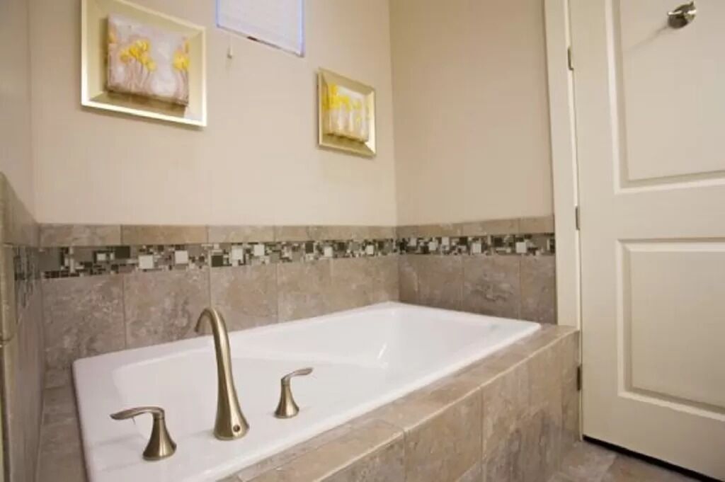 A bathroom with a large bathtub, two faucets, and a tiled backsplash.