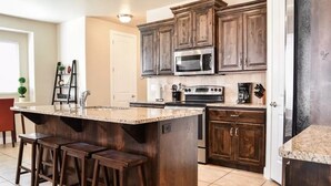 A kitchen with dark wooden cabinets, a granite countertop, a stainless steel oven, and a coffee maker. - Solana Linda (Washington)