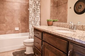 A bathroom with a bathtub, toilet, vanity with a sink, and a mirror.