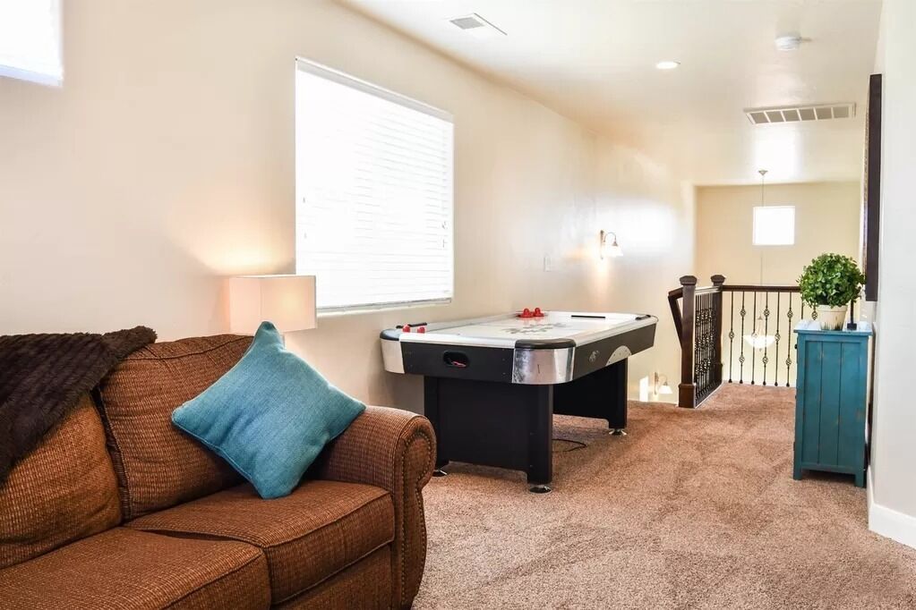 A cozy living room with a brown couch, a foosball table, and a staircase leading to an upper level.