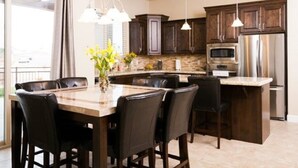 Una cocina moderna con armarios de madera oscura, una isla central con asientos, horno empotrado e iluminación colgante.