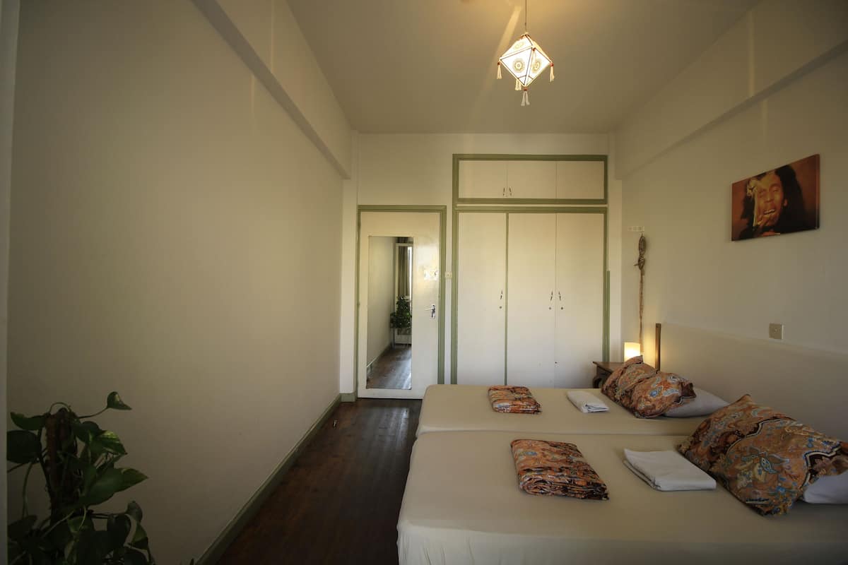 A hotel room with a bed, a bedside table, a hanging light fixture, and a door leading to another room.