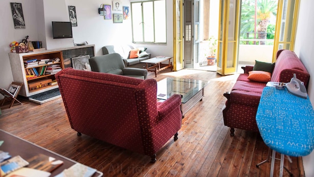 A living room with a sofa, armchair, coffee table, and an ironing board.