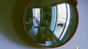 A round mirror reflecting a room with a window, a door, and some furniture.