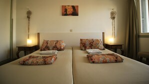 A hotel room with two beds, patterned pillows, bedside lamps, a wall hanging, and a window with curtains.