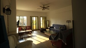 A spacious living room with a ceiling fan, a glass coffee table, a blue sofa, and a red armchair.