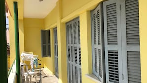 A corridor with yellow walls and grey shutters, a metal rack with clothes, and a ceiling-mounted security camera.