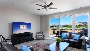 Ein Wohnzimmer mit Flachbildfernseher, Ledersofas, einem Couchtisch und Deckenventilator.